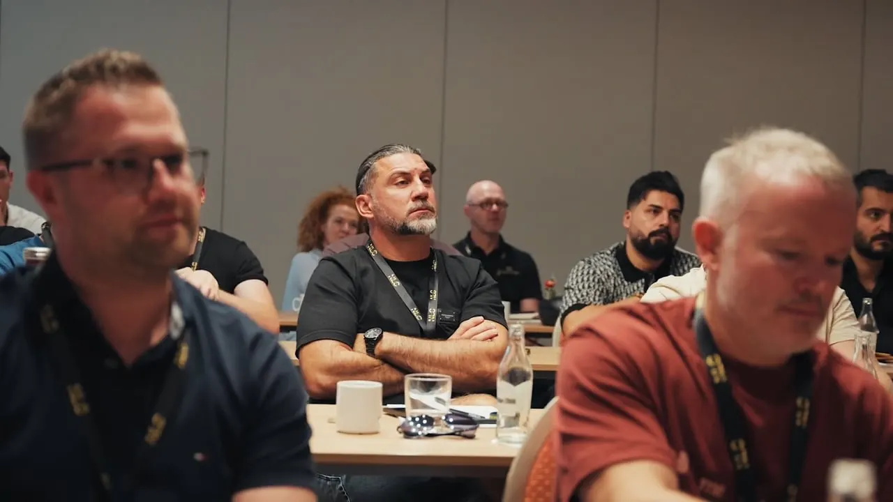 Teilnehmer sitzen an Tisch während Mastermind-Session, Fokus auf mehrere Männer in Vordergrund
