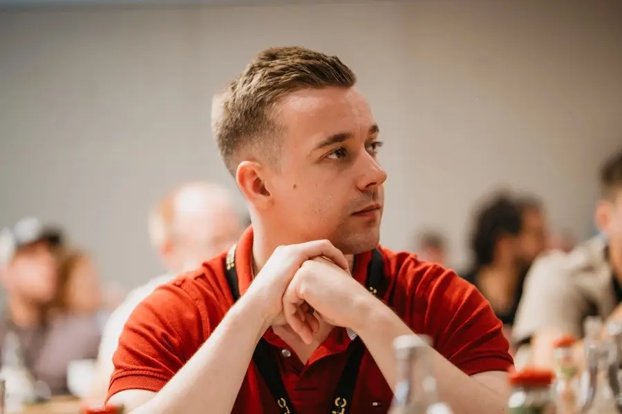 Junger Mann in rotem Shirt mit NLC-Badge, nachdenklich während Stammtisch-Diskussion