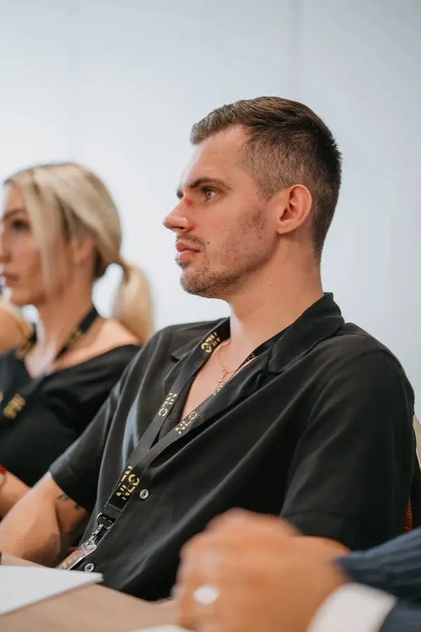 Junger Mann mit schwarzem NLC-Shirt und Badge in konzentrierter Pose bei Live-Session