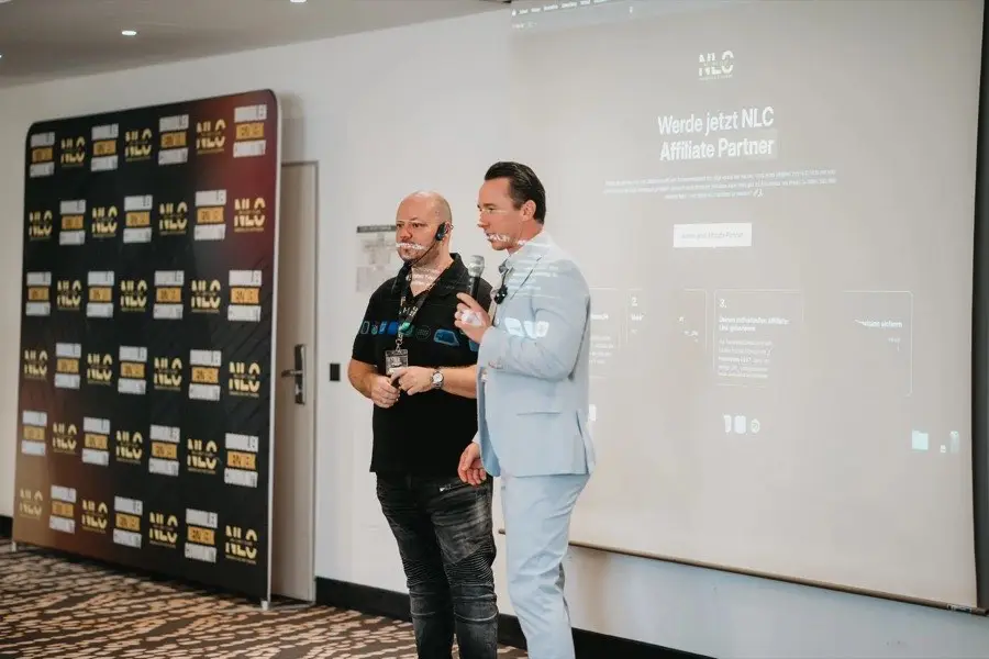 Zwei Männer auf Bühne beim NLC Day mit Backdrop und Präsentation