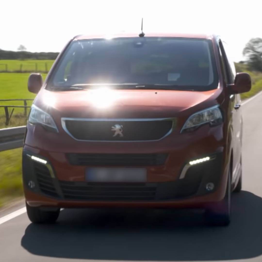 Peugeot Traveller in Rot-Braun von vorne fotografiert auf einer Landstraße mit Feldern im Hintergrund