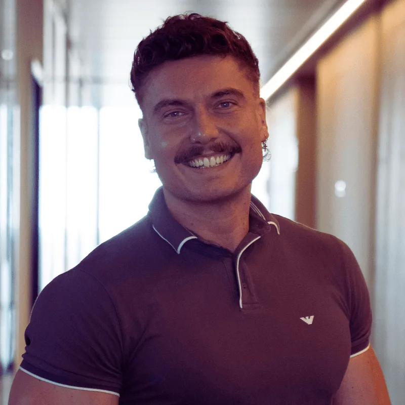 Porträt Enrico Schuch mit breitem Lächeln, Polo-Shirt in Flur mit Neonlicht