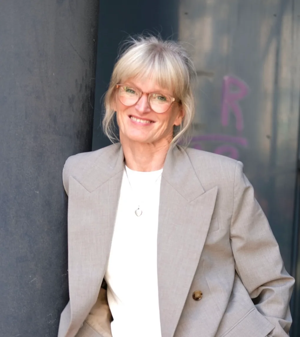 Porträt Kirsten Nachtigall mittleres Alter, weiße Haare, Brille, beiger Blazer vor Betonwand