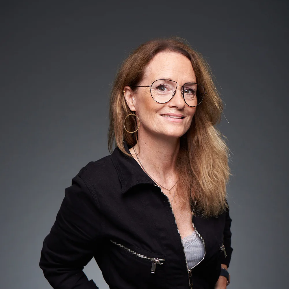 Stefanie Krüll, Frau mit braunen Haaren, Brille und Ohrringen in schwarzer Jacke vor grauem Hintergrund