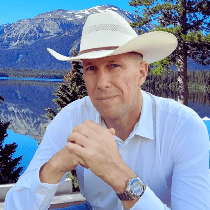 Tom Kaules, Mann mit Cowboyhut in weißem Hemd vor Bergsee-Landschaft