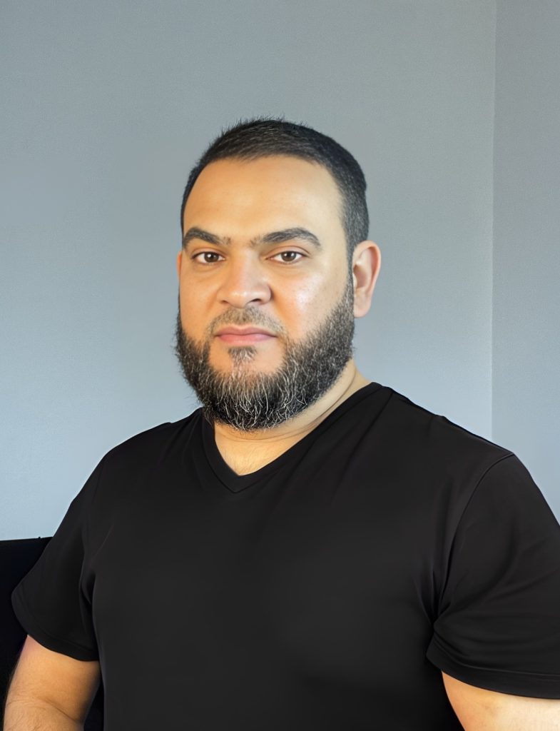 Porträt Muhammad Asmal mit Bart, schwarzes T-Shirt, grauer Hintergrund