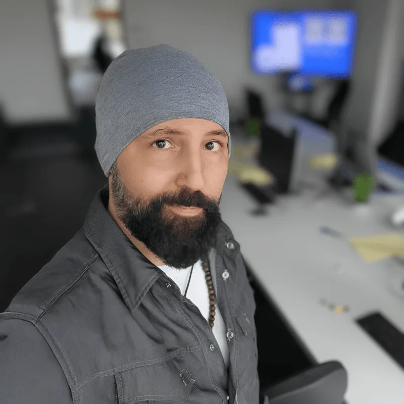 Porträt Engin Senli mit grauer Mütze und Bart, modernes Büro im Hintergrund