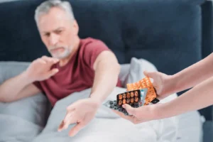 Älterer Mann lehnt Medikamente ab, Frau hält Tabletten an