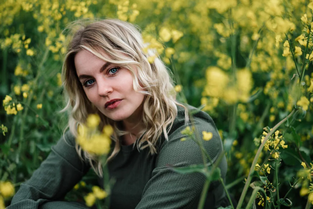 Blonde Frau in grünem Oberteil zwischen gelben Blumen bearbeitet