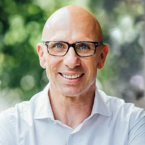 Mann mit Brille und weißem Hemd vor unscharfem grünem Hintergrund