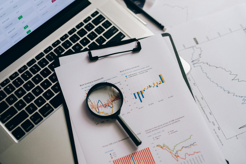 Laptop mit Datenanalyse-Charts, Lupe über Grafik, Kopfhörer und ausgedruckte Statistiken auf Schreibtisch