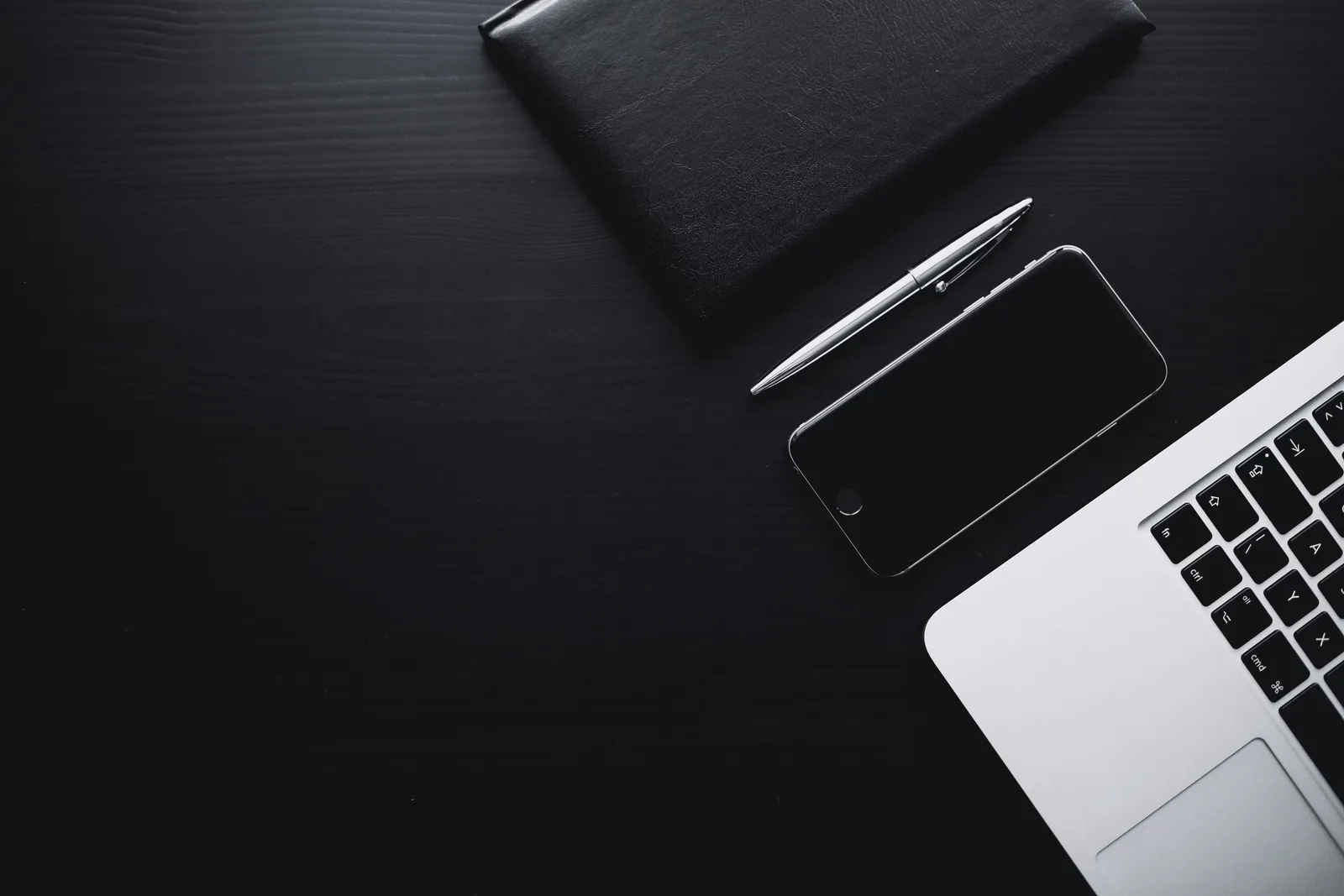 Flat-Lay Workspace mit Laptop, Smartphone, Stift und schwarzer Ledermappe auf dunklem Hintergrund