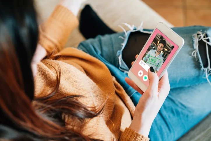 Frau mit rotbraunem Haar hält Smartphone mit Dating-App und Like-Interface