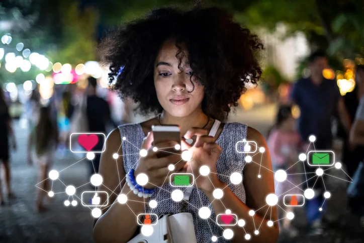Frau mit Afro-Frisur hält nachts Smartphone mit Social-Media-Icons