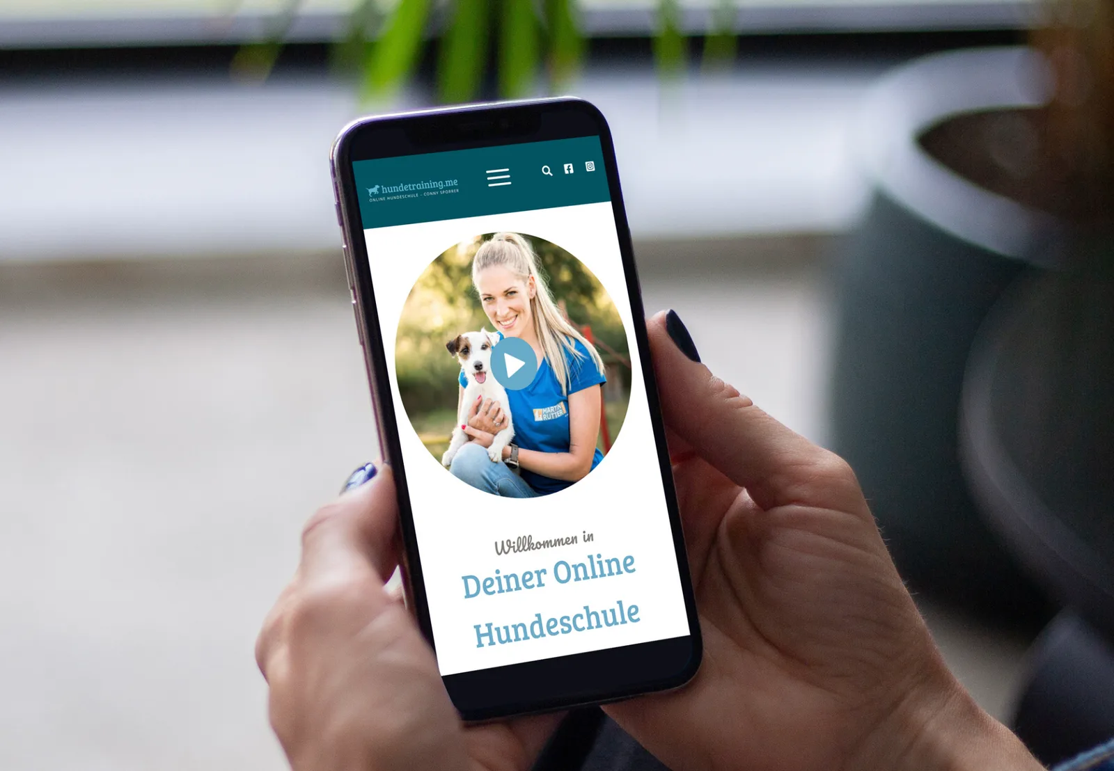 Smartphone zeigt Website der Online Hundeschule mit Trainerinnen-Foto und Play-Button