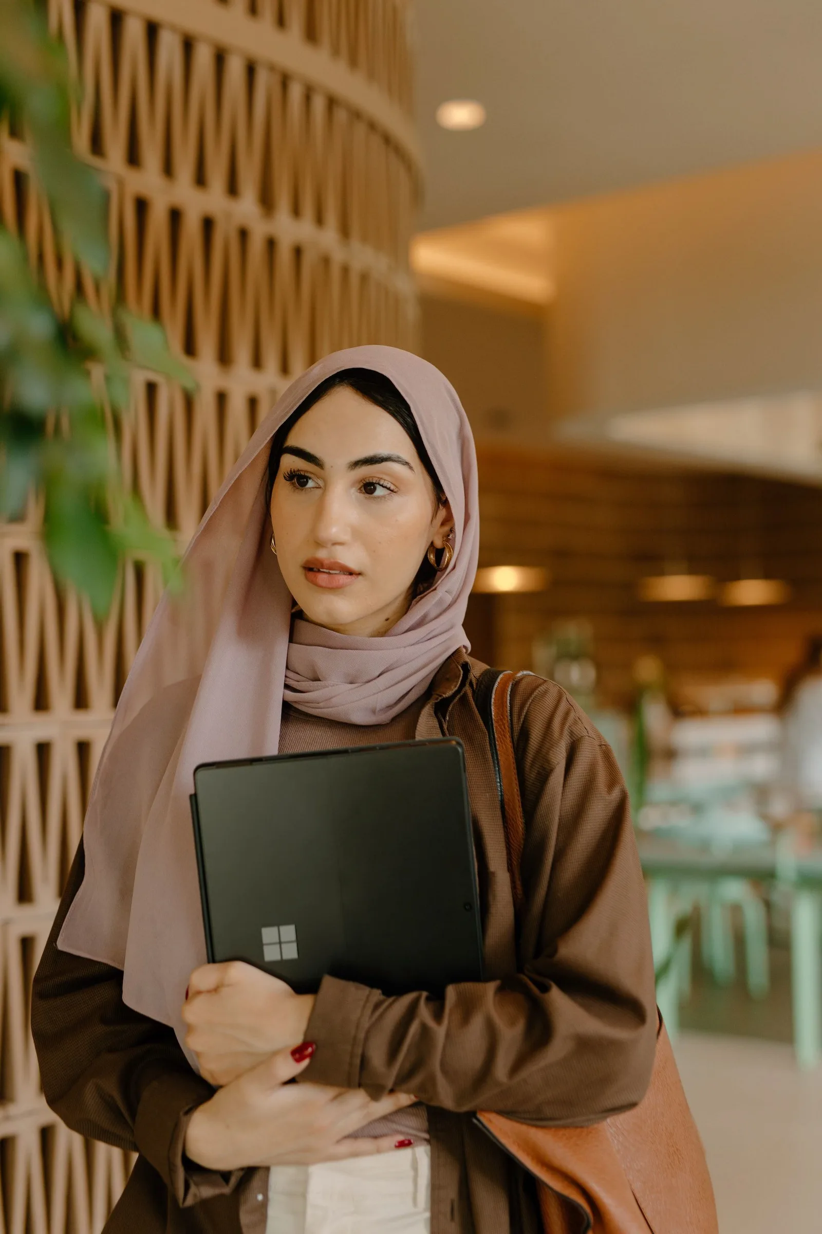 Frau mit Kopftuch hält Microsoft-Tablet in modernem Büro-Interieur mit Holzdetails