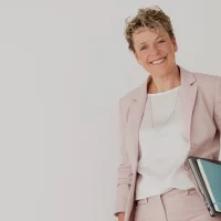 Britta Wein, Frau in beigem Blazer und weißem Top, lächelnd