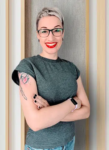 Lena Kössner mit Brille, grauem T-Shirt und Tätowierung am Arm