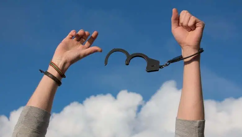 Zwei Hände mit zerbrochenen Handschellen vor blauem Himmel