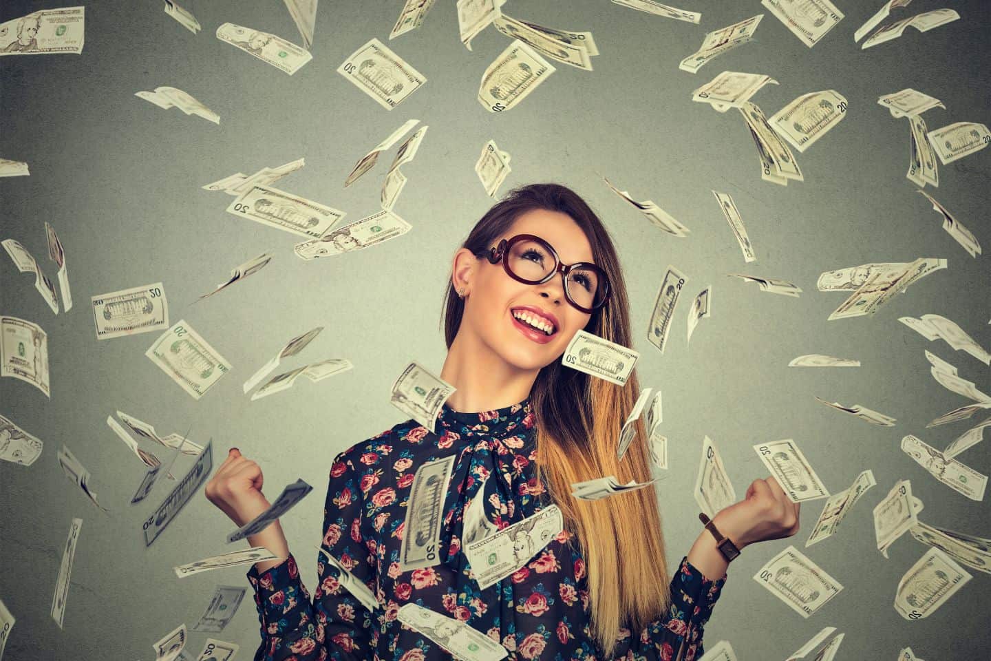 Junge Frau mit Brille und Blumenshirt umgeben von fallenden Dollarnoten