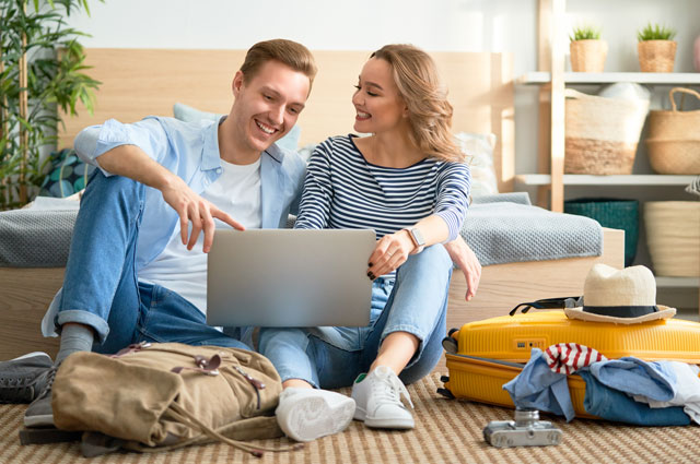 Original Birkenbihl-Sprachkurs Englisch für Urlaub & Reise 7 Junges Paar sitzt auf Boden mit gepackten Koffern und plant Reise am Laptop
