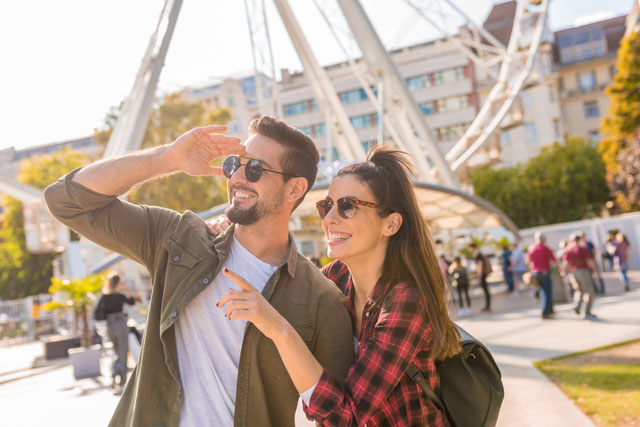 Original Birkenbihl-Sprachkurs Englisch für Urlaub & Reise 9 Mann und Frau mit Sonnenbrille schauen auf Sehenswürdigkeit mit Riesenrad im Hintergrund