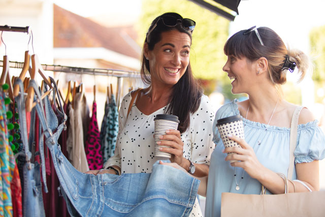 Original Birkenbihl-Sprachkurs Englisch für Urlaub & Reise 10 Zwei Frauen beim Shopping an sonnigem Tag, betrachten Kleidung auf Ständer