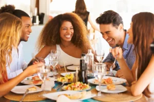 Gruppe von fünf Personen sitzt lachend beim Essen zusammen am Tisch
