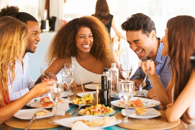 Gruppe von fünf Personen sitzt lachend beim Essen zusammen am Tisch