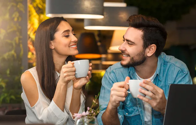 Junges Paar trinkt Kaffee und unterhält sich lächelnd in moderner Café-Atmosphäre