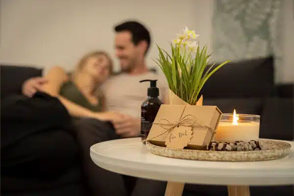 Paar entspannt auf Sofa mit Magoody Geschenkbox, Kerze und Pflanze im Vordergrund