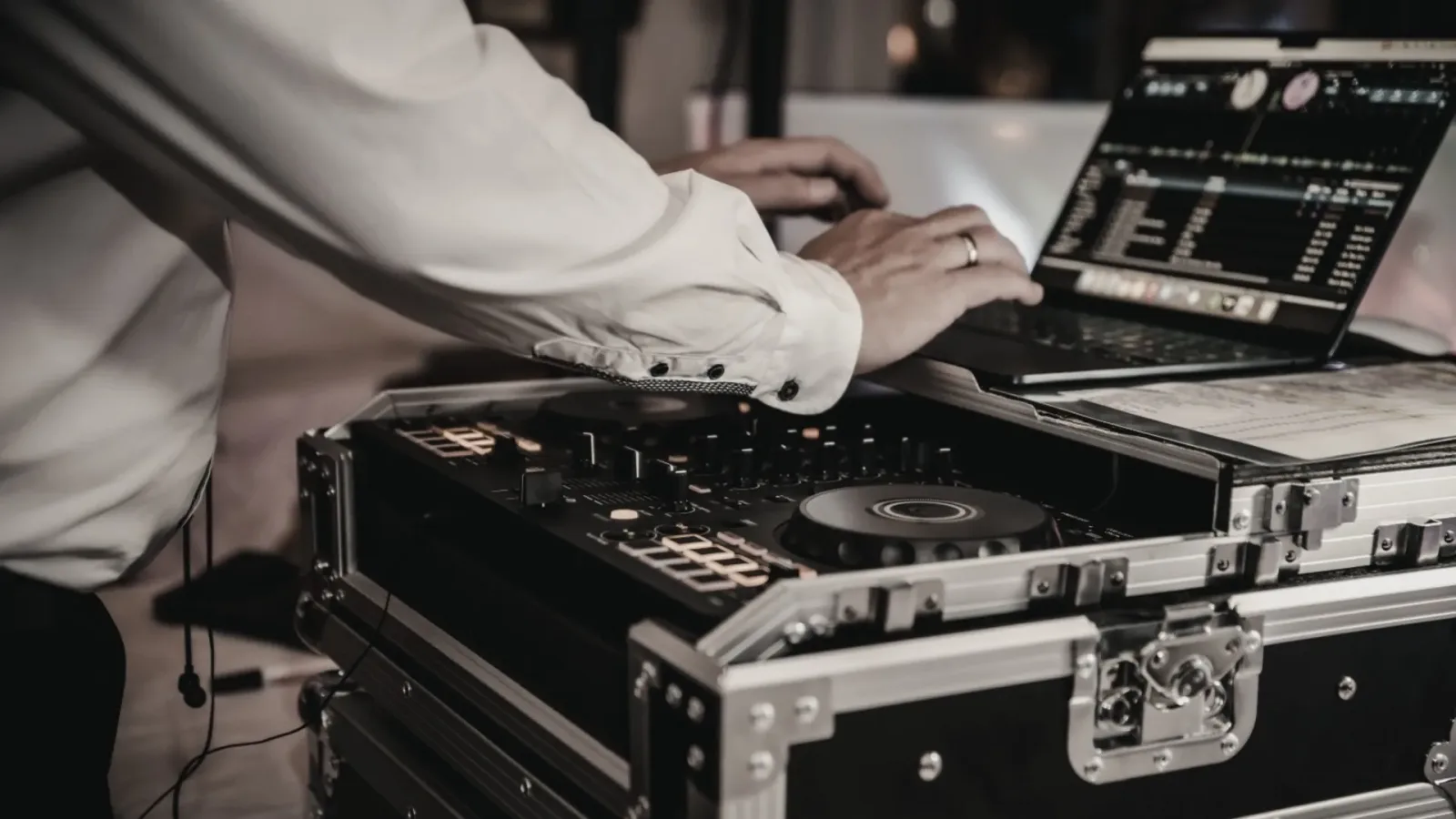 DJ in weißem Hemd arbeitet am Mischpult mit Laptop, nutzt das Setbook für Songauswahl