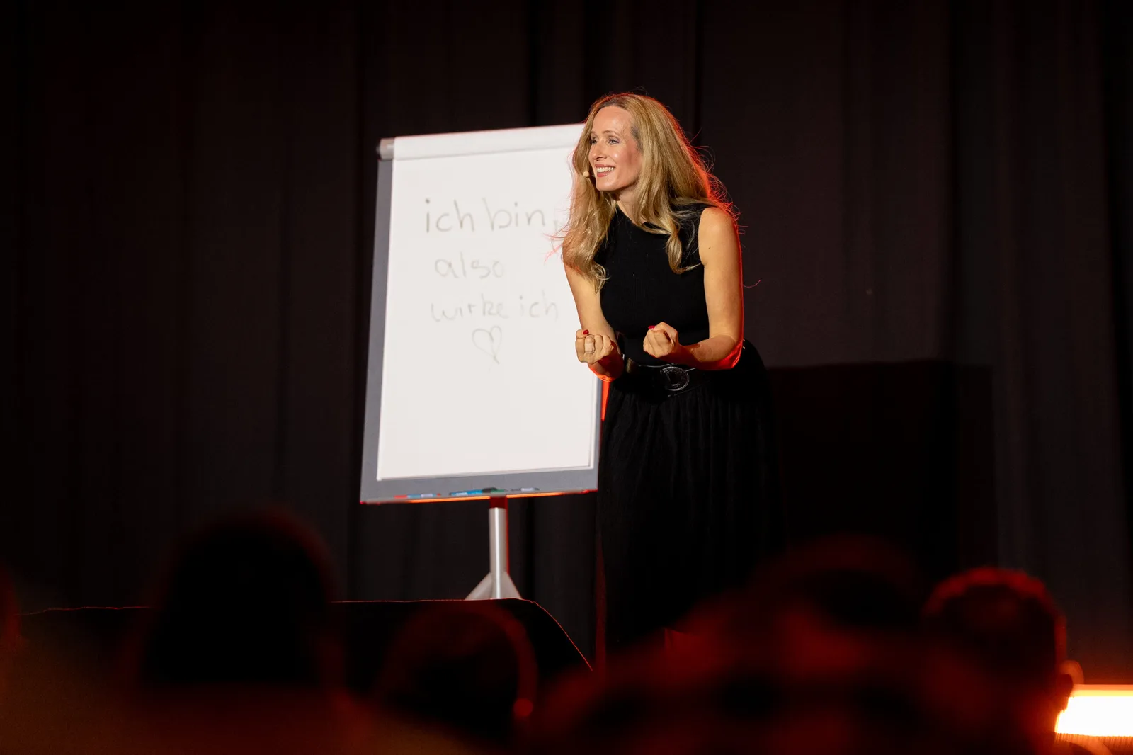 Passionate Business Club – Gruppencoaching für Coaches 7 Annabell Whitney auf Bühne vor Flipchart, schwarzer Anzug, Coach in Präsentationssituation