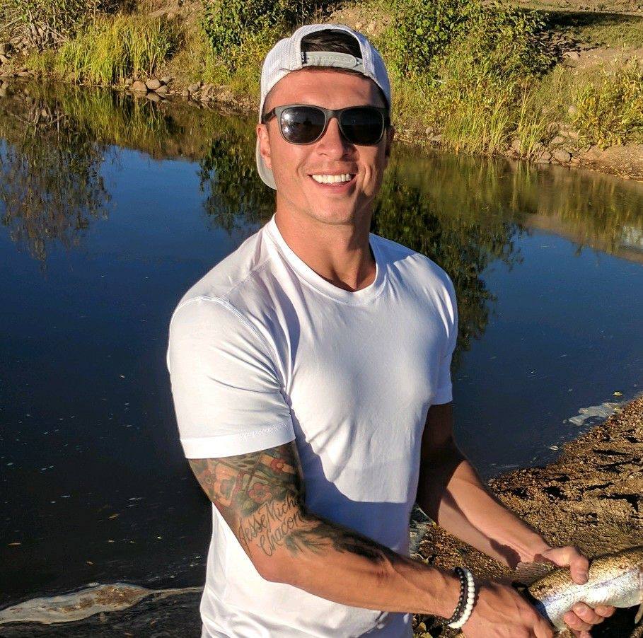 Mann mit weißem T-Shirt und Cap am Fluss, Fisch in der Hand