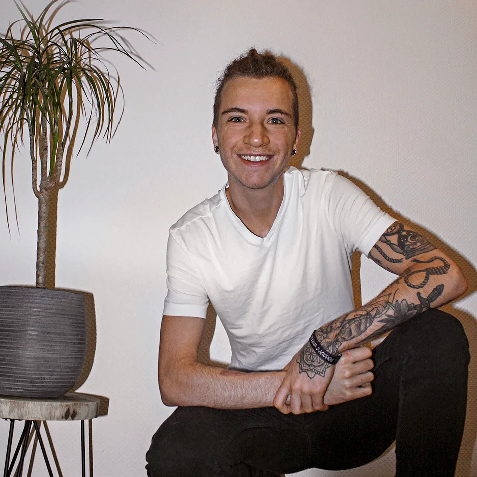 Portrait von Christian Dänzer, lächelnder junger Mann in weißem T-Shirt mit Tätowierungen