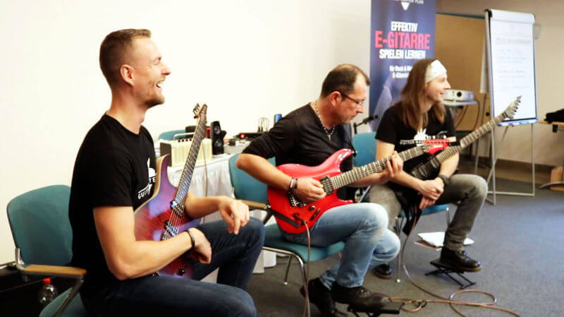 Drei Gitarristen spielen E-Gitarren während Live-Workshop Demonstration