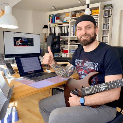 Mann mit Gitarre in Heimstudio vor Laptop, Daumen hoch