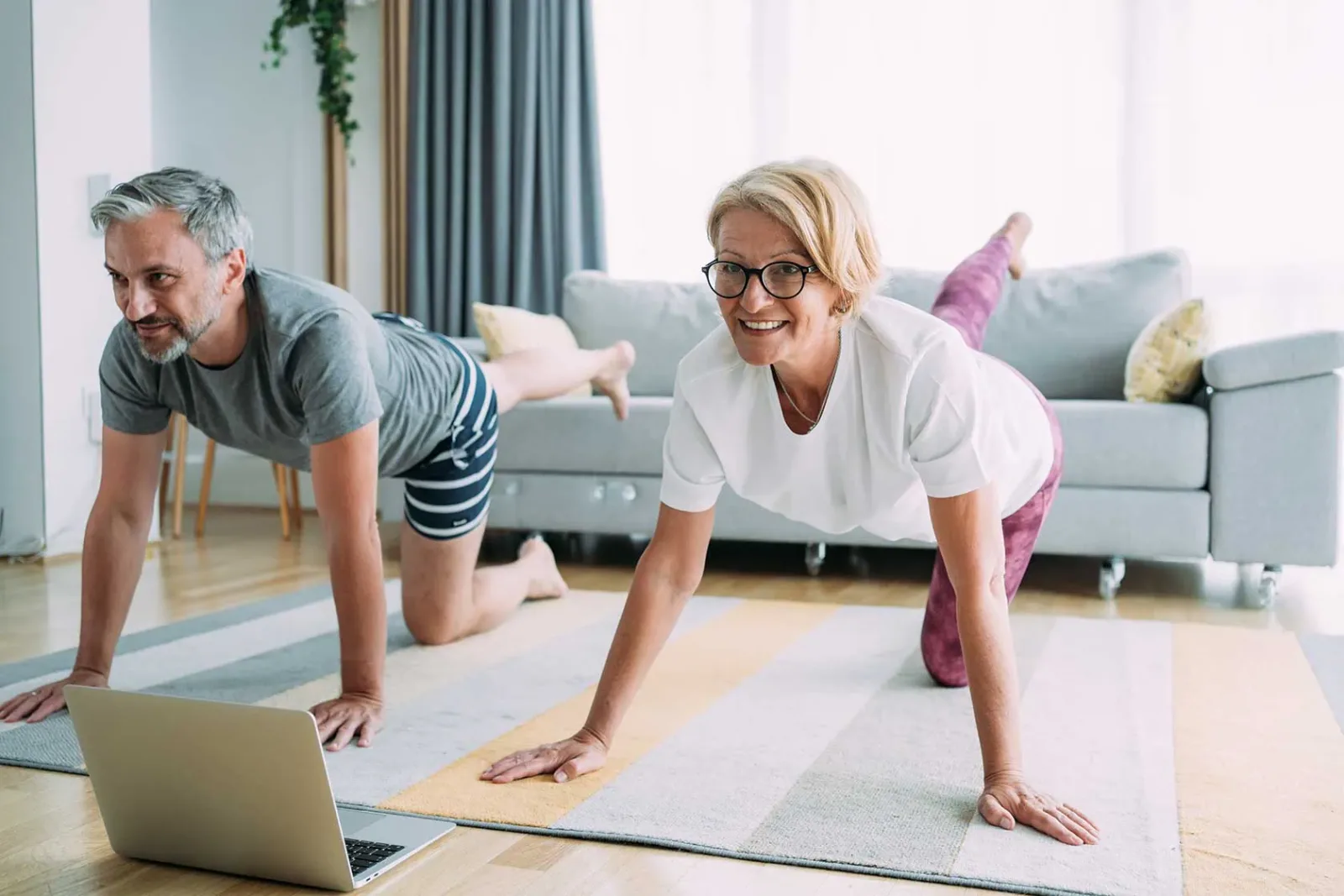 Mittelalter Paar macht Plank-Übung lachend auf Trainingsmatte vor Laptop