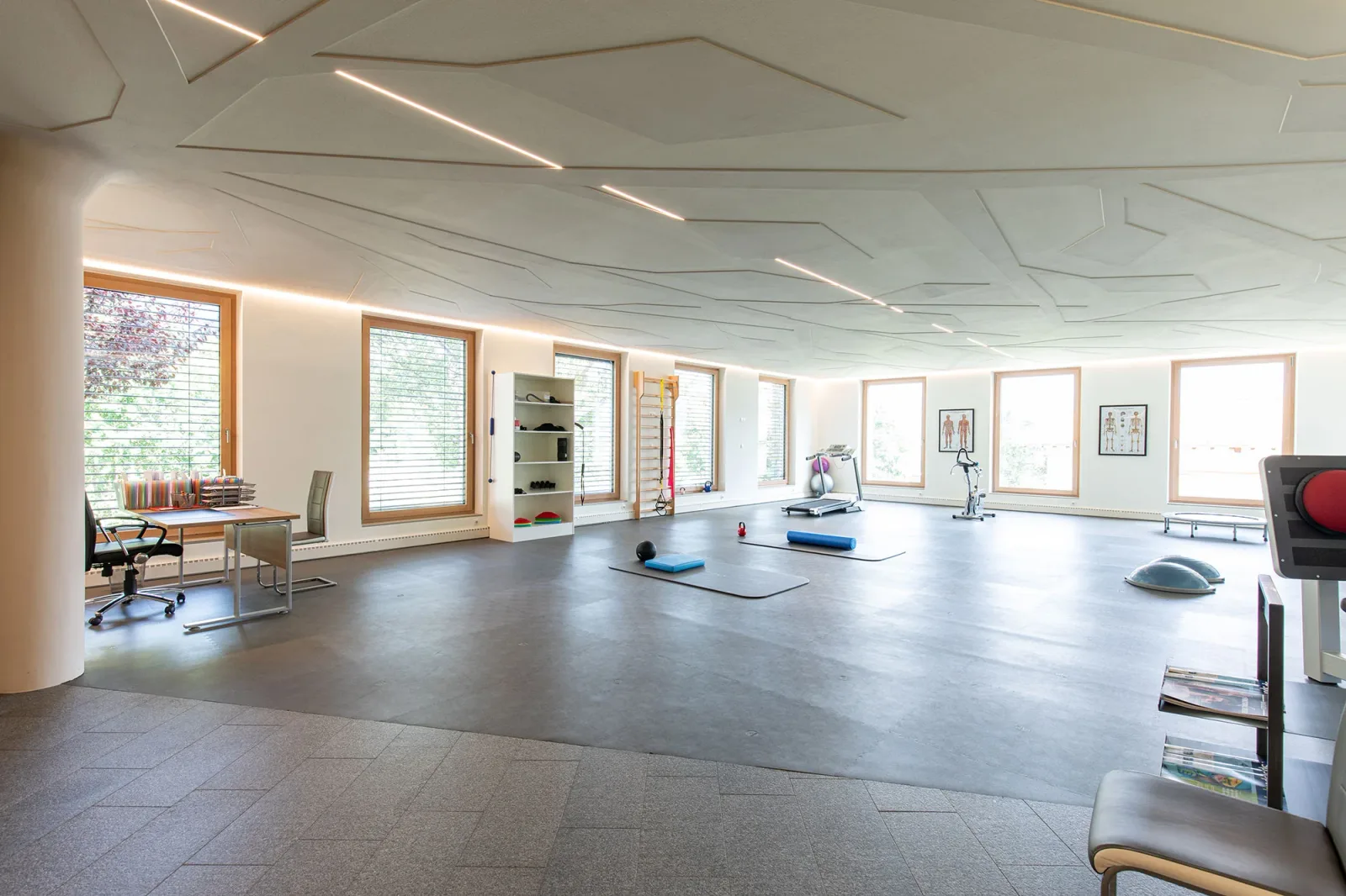 Helles Pilates-Studio mit Matten, Geräten, großen Fenstern und Bürobereich