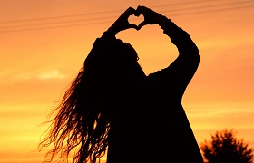 Silhouette einer Person formt Herzform gegen Sonnenuntergang