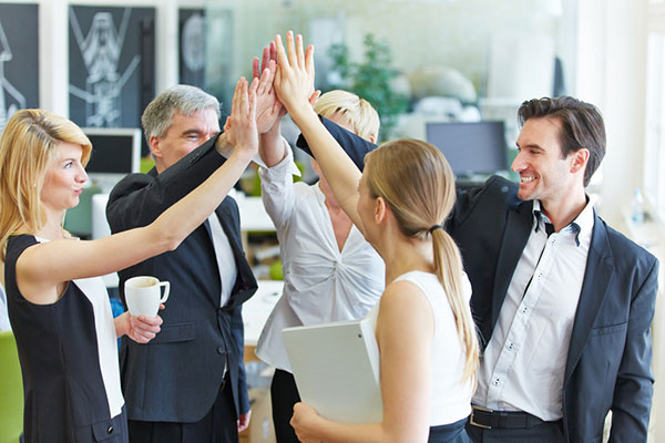 Geschäftsteam verschiedener Altersgruppen macht hochmotiviert ein High-Five im modernen Büro