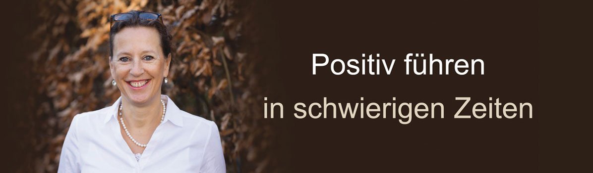 Antje Heimsoeth in weißer Bluse vor braunem Naturhintergrund mit Text "Positiv führen in schwierigen Zeiten"