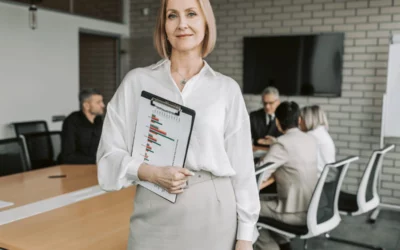 Frau im Büro mit Tablet und Team im Hintergrund, Change Management