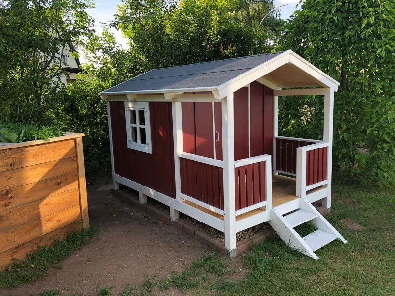 Fertig gebautes Spielhaus rot-weiß mit Veranda und Treppe im Garten