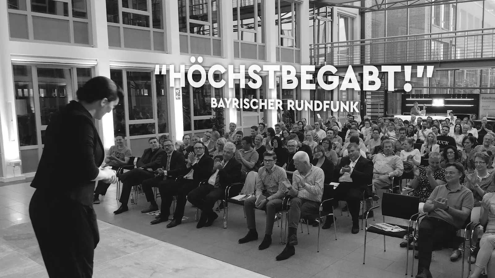 Profiler Suzanne präsentiert vor großem Publikum in moderner Halle, Text 'HÖCHSTBEGABT!' und 'BAYRISCHER RUNDFUNK' überlagert