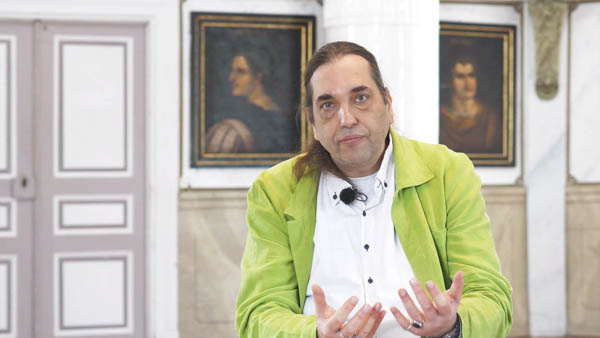Stefan H. in neongelber Jacke gestikulierend vor historischem Interieur