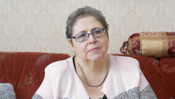 Porträt einer Frau mit Brille und Halskette, ernster Blick, auf Sofa sitzend