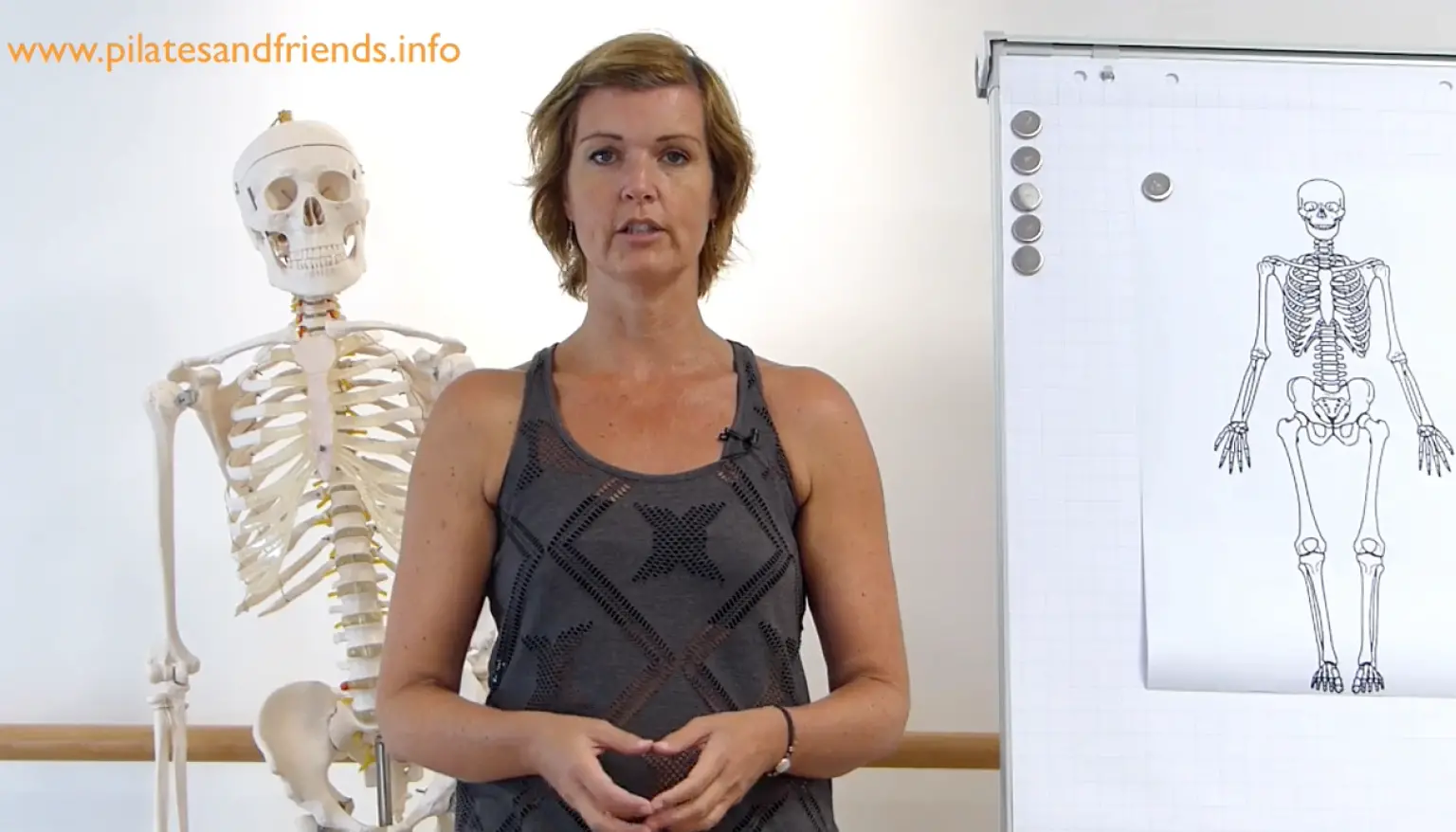Instruktorin mit Skelettmodell und anatomischem Poster, Website-URL sichtbar
