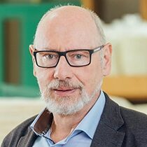 Prof. Amann Jennson mit Brille und grauem Bart auf unscharfem Hintergrund