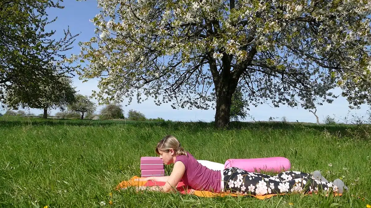 Frau in Yin-Yoga-Position auf farbigem Tuch unter Kirschbaum